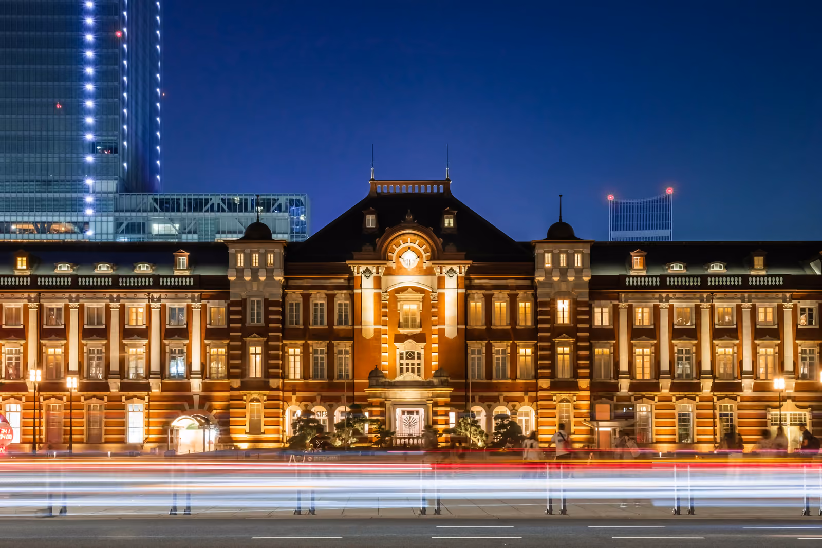 La façade de brique rouge de la gare de Tokyo, côté Marunouchi, illuminée de nuit avec des traînées de phares au premier plan
