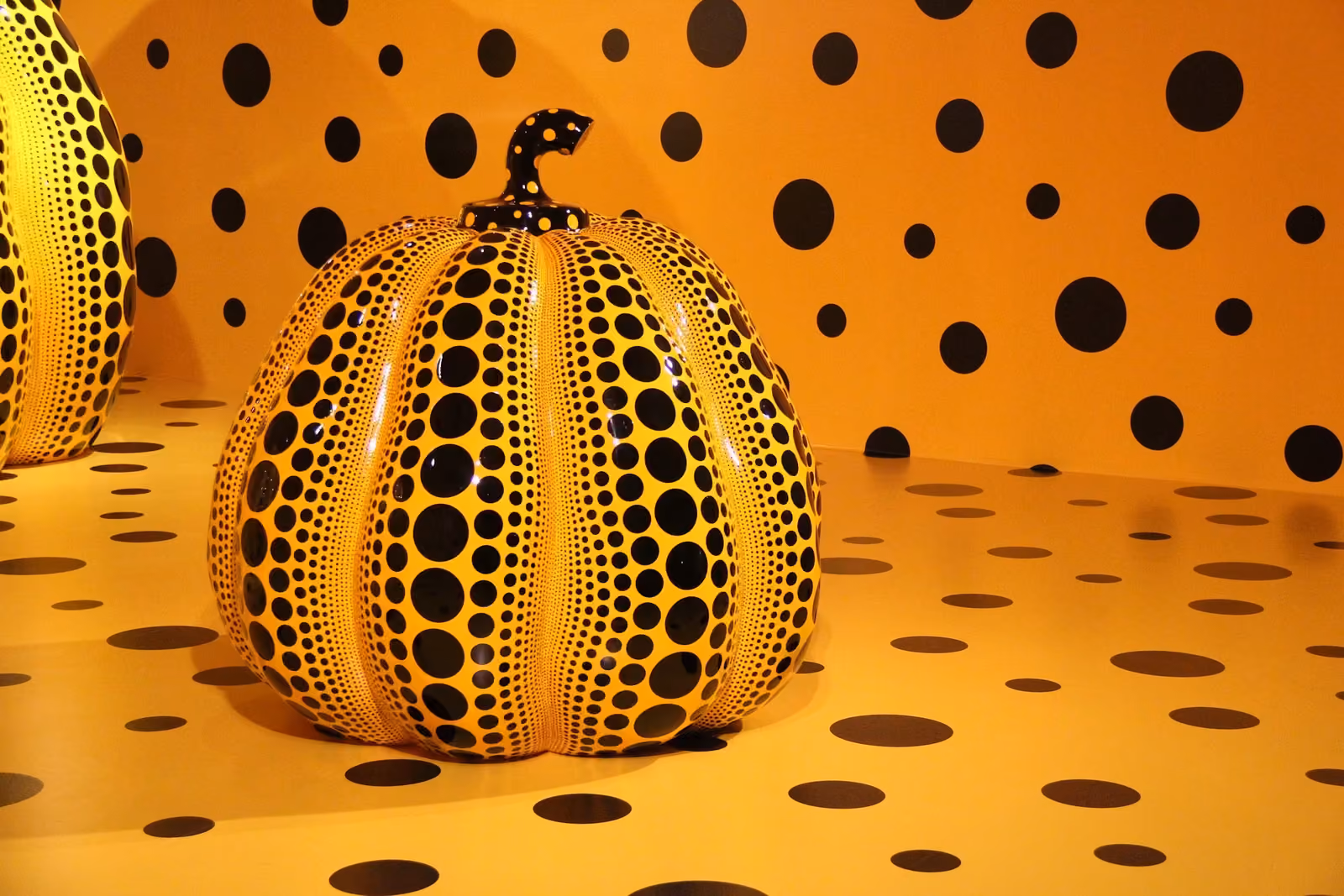 Une citrouille jaune à pois noirs de Yayoi Kusama, dans une salle aux murs et au sol couverts des mêmes pois