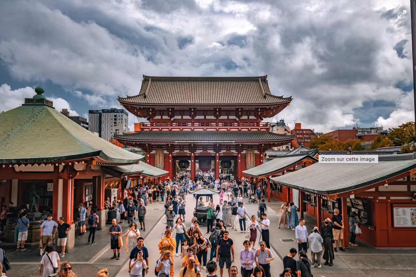 La grande porte rouge du Senso-ji, à Asakusa, au bout de l'allée Nakamise remplie de visiteurs sous un ciel nuageux