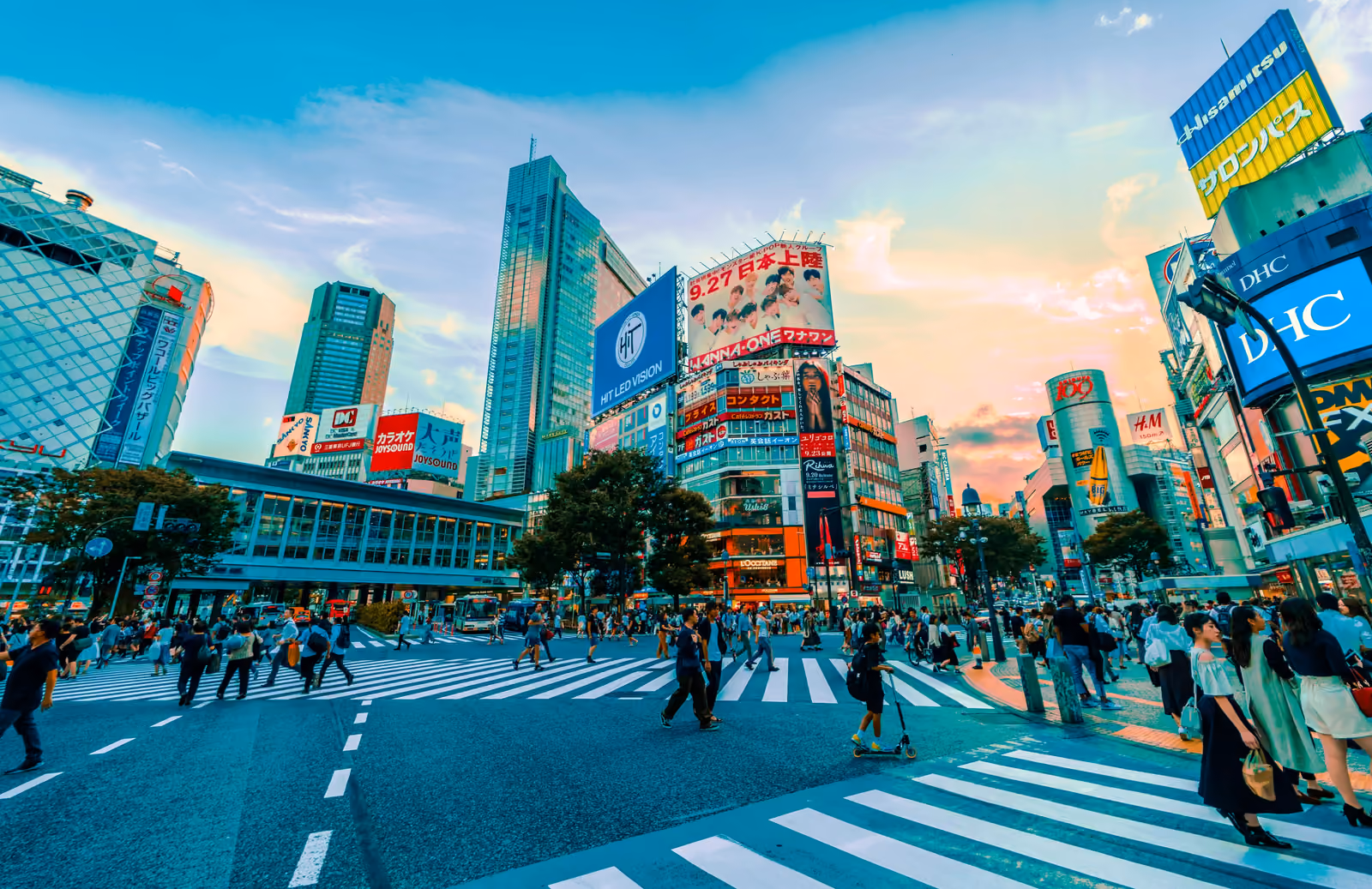 Le carrefour de Shibuya et ses passages piétons, entourés d'écrans géants et de tours, au coucher du soleil