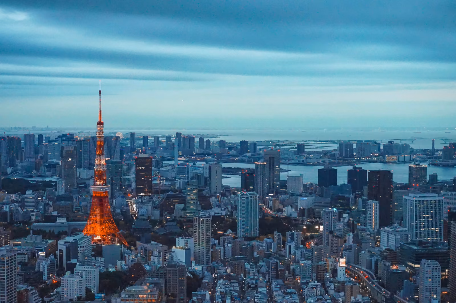 La Tokyo Tower illuminée en orange au crépuscule, entourée des immeubles de Minato, avec la baie de Tokyo au loin