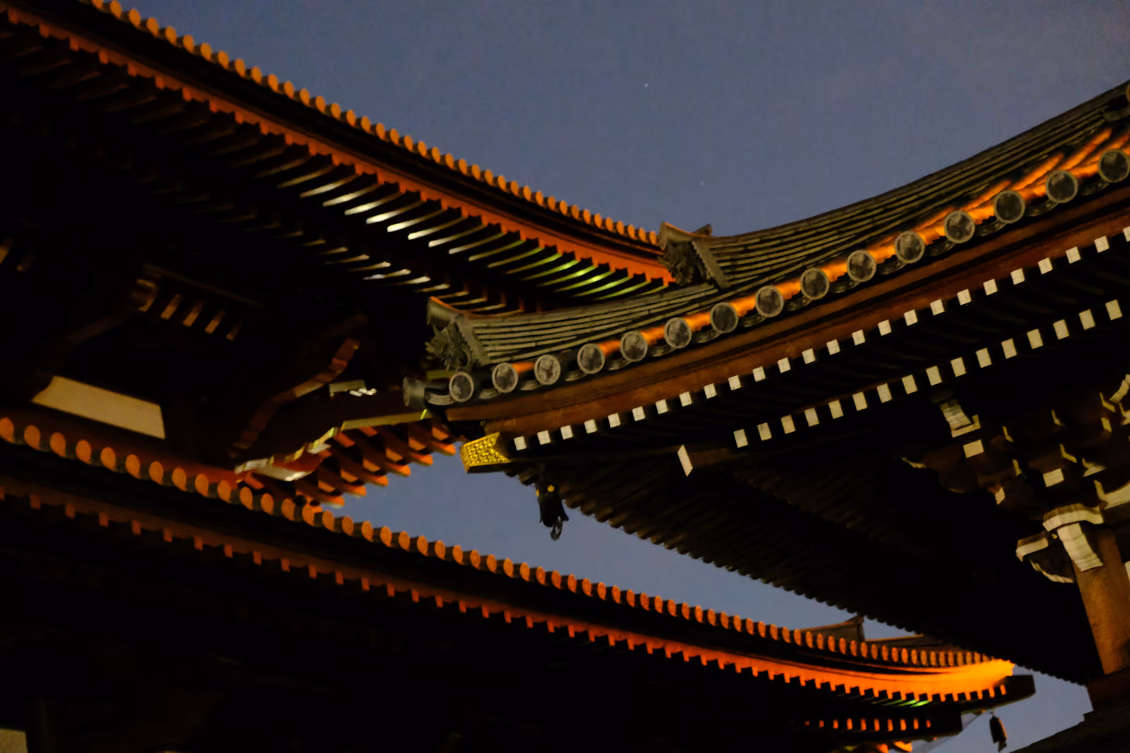 Les toits superposés du temple Zojo-ji illuminés la nuit, leurs avant-toits soulignés d'orange sur le ciel sombre