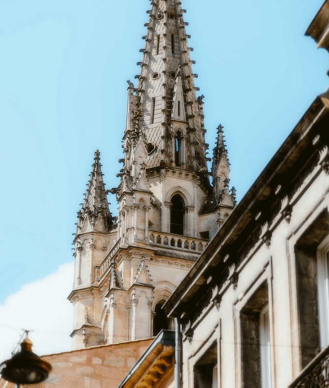 Flèche gothique de la Basilique Saint-Michel à Bordeaux, avec son architecture richement ornée, vue sous un ciel bleu clair.