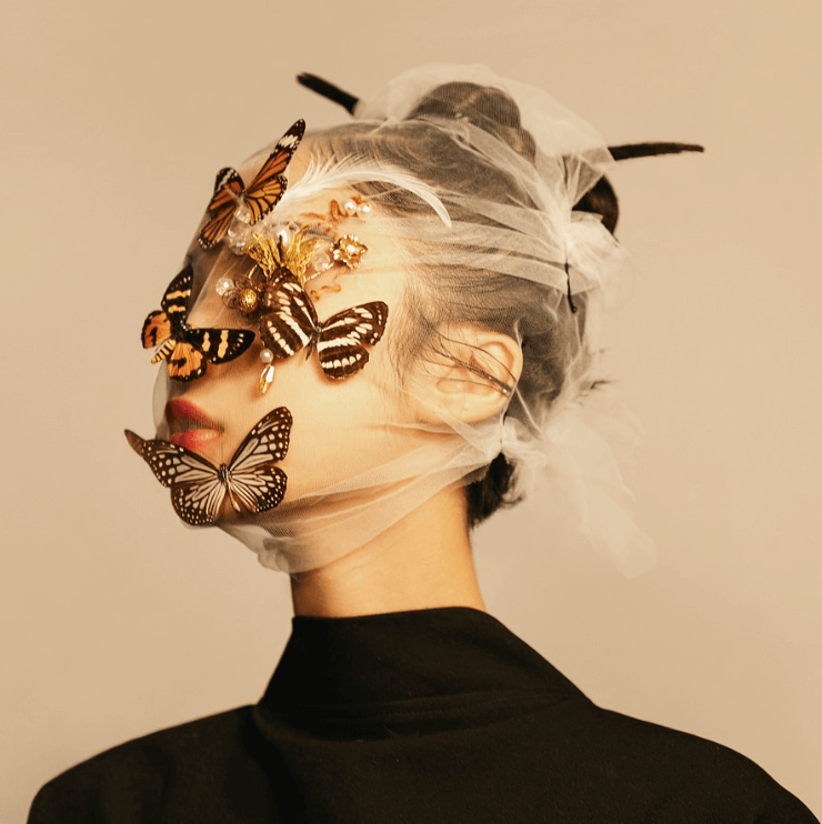 Portrait artistique d'une femme portant un voile transparent décoré de papillons et d'ornements dorés, illustrant une esthétique contemporaine et onirique, avec des tons doux et minimalistes.