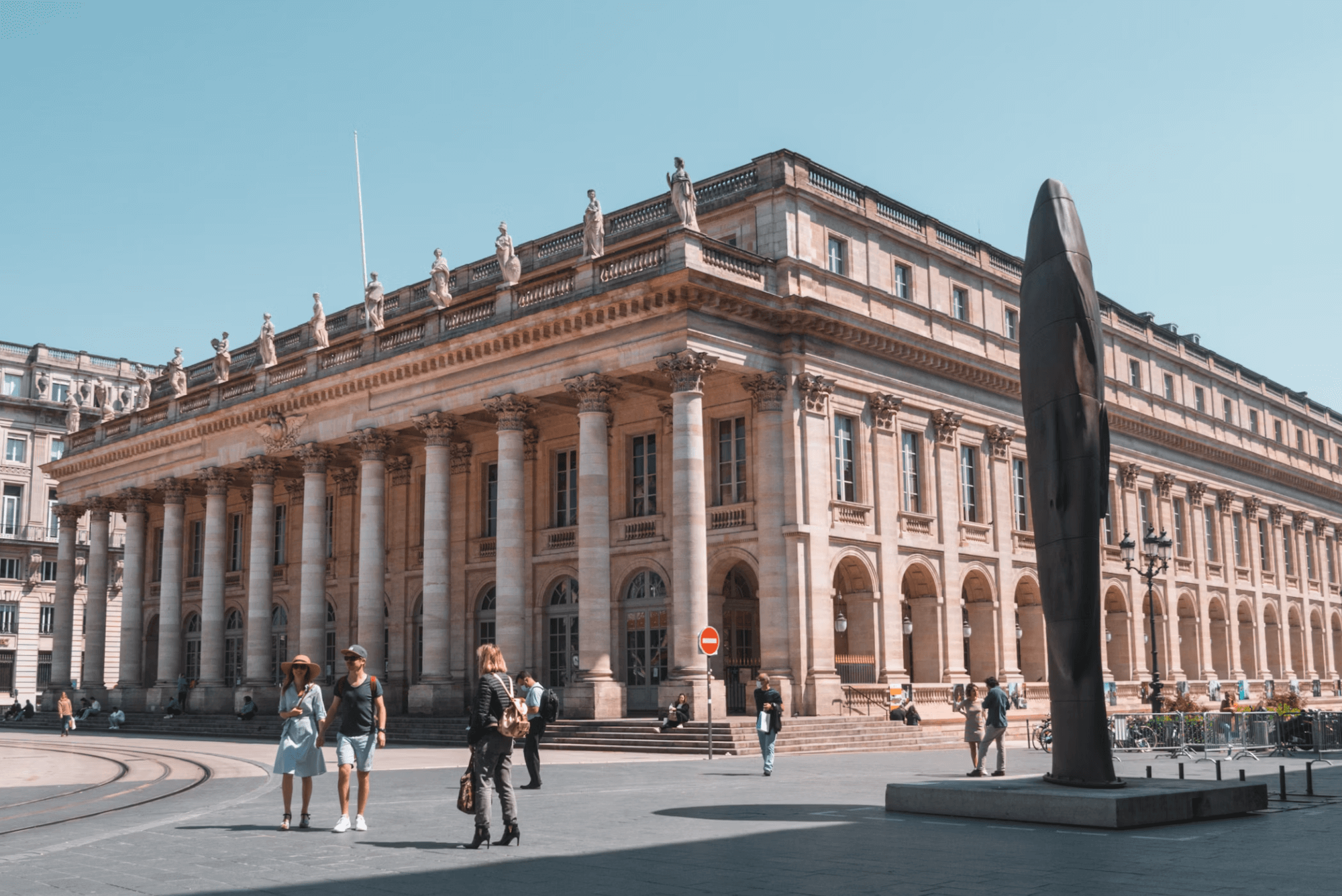 Façade monumentale du Grand Théâtre de Bordeaux, avec ses colonnes corinthiennes et statues emblématiques, sous un ciel dégagé.