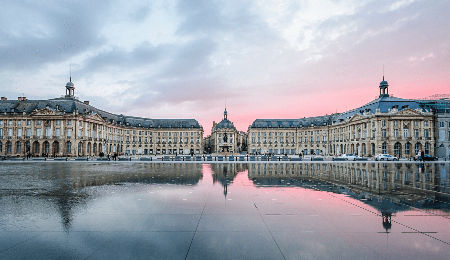 Vue emblématique de la Place de la Bourse à Bordeaux, avec ses façades néoclassiques et le reflet dans le Miroir d’eau par une journée ensoleillée.