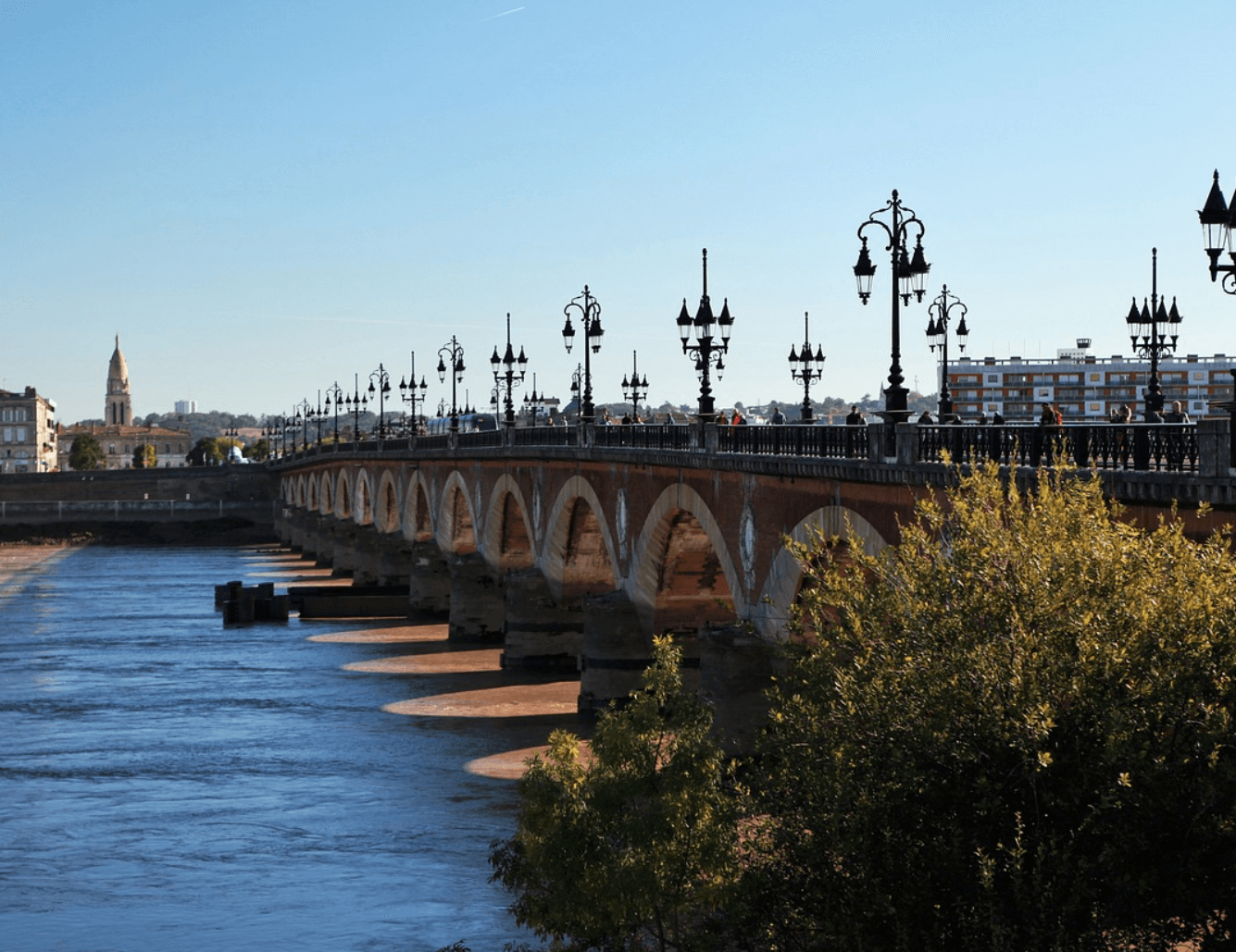 Vue panoramique du Pont de Pierre à Bordeaux, avec ses arches emblématiques s’étendant au-dessus de la Garonne, capturé sous un ciel dégagé.
