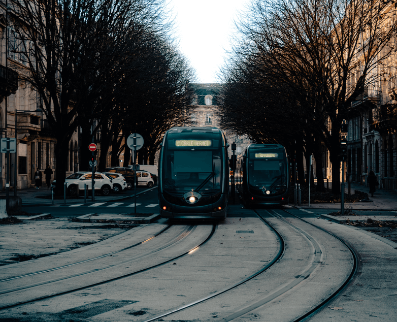 Tramway circulant entre une allée d’arbres majestueux sur des trottoirs bordant des immeubles typiques de Bordeaux, sous un ciel bleu clair, illustrant le charme et la modernité du transport urbain dans cette ville historique.