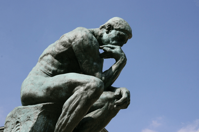 Une statue représentant un homme nu assis sur un rocher, la tête appuyée sur sa main dans une posture pensive