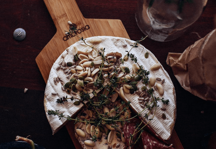 Camembert entamé sur une planche en bois, garni de cacahuètes et d’herbes.