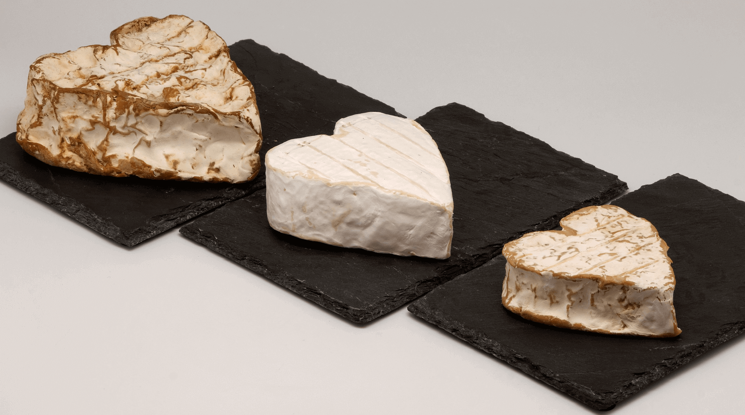 Trois fromages Neufchâtel en forme de cœur, alignés verticalement sur une planche noire.