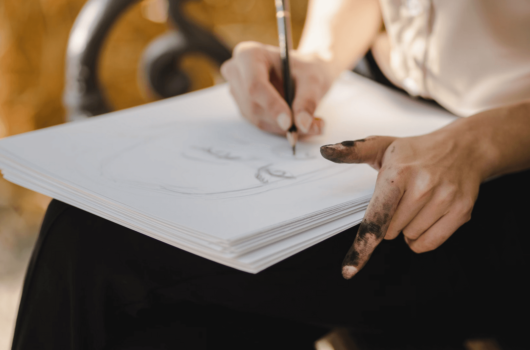Une femme tenant des feuilles blanches. Elle est entrain de dessiner un visage aux crayons